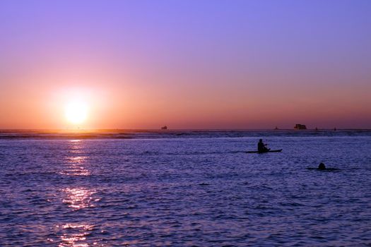 People and boats in the water during Sunset over the ocean at Ala Moana Beach Park on Oahu, Hawaii.