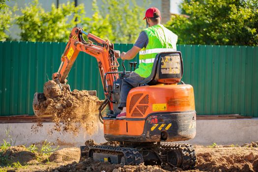 A man on a mini-excavator levels a piece of land, loosens the soil