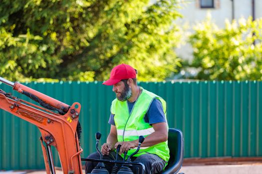 A man on a mini-excavator levels a piece of land, loosens the soil