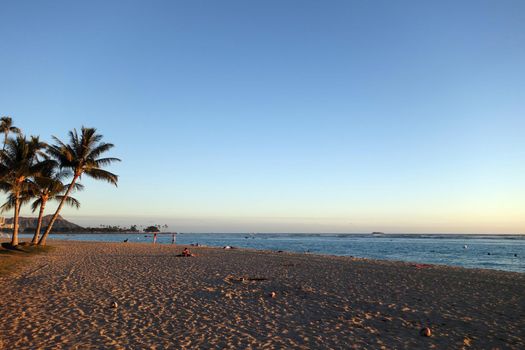 People hang out at Ala Moana Beach Park at Dusk with iconic Diamondhead in the distance during a beautiful day on the island of Oahu, Hawaii. 