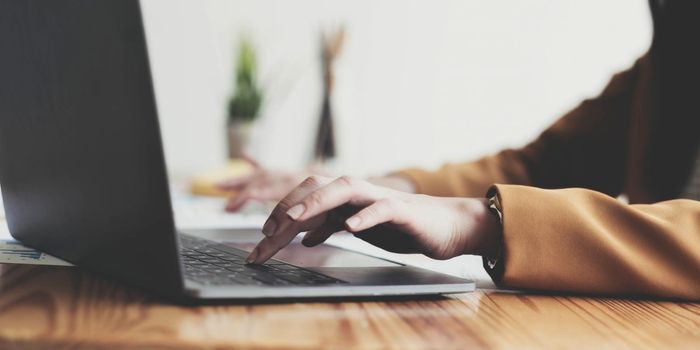 Side view of businesswoman's hands using laptop computer placed on messy office desktop.