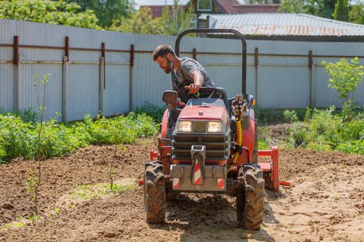 A man on a mini-excavator levels a piece of land, loosens the soil