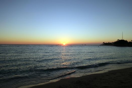 Sunset on as wave lap on the beach from the ocean at Ala Moana Beach Park on Oahu, Hawaii.