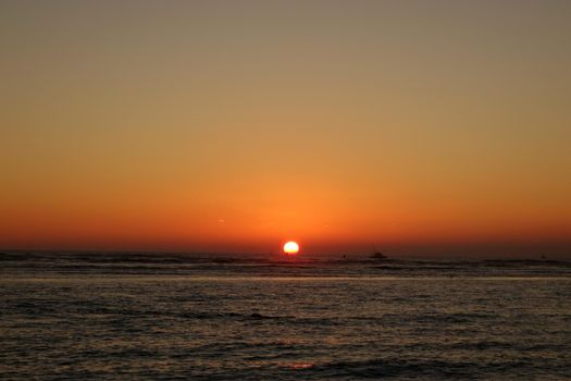 boats and buoy in the water during Sunset over the ocean at Ala Moana Beach Park on Oahu, Hawaii.