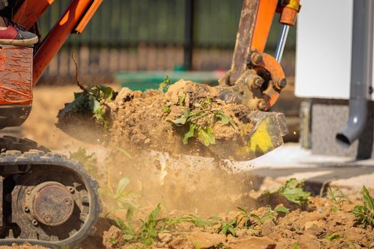 A mini excavator with a rake loosens the ground. landscape preparation