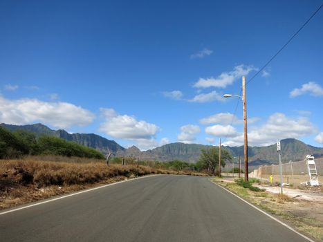 Long empty road in Maili Valley next to Naval Magazine and mountains in the distance on Oahu, Hawaii.