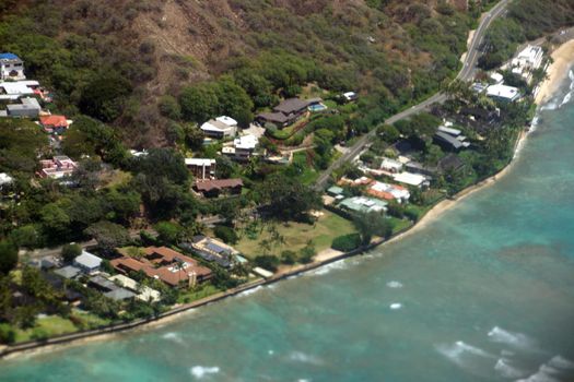 Aerial view of slopes of Diamond Head crater with road surrounded by Luxury homes, Leahi Beach Park, and the shallow ocean waters off shore of the pacific ocean on Oahu, Hawaii on a beautiful day. 