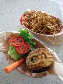 Open Face Hawaiian style burger with pineaple topping, lettuce, tomatoes, carrot with side of French fries.