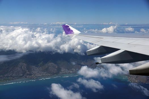 HONOLULU, JUNE 26: Wing of Hawaiian Airlines plane flying in the air above Honolulu, Hawaii and clouds on June 26, 2015.