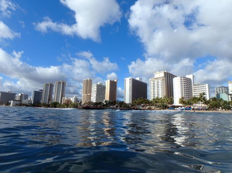 Waves lap towards Queens Beach and pier in Waikiki with Hotels in the distance.  Seen from water.