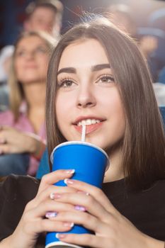 Favorite leisure hobby. Vertical closeup of a gorgeous brunette woman drinking watching movies at the cinema smiling happily