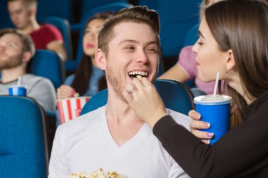 Bon appetit! Closeup shot of a young woman feeding her cheerful laughing man with popcorn at the movie theatre