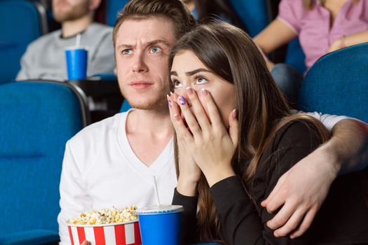 What the hell? Portrait of a disturbed young handsome man hugging his scared girlfriend while watching movies at the cinema