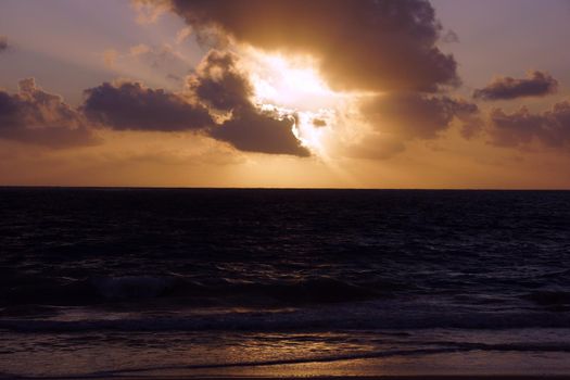 Early Morning Sunrise on Waimanalo Beach over ocean bursting through the clouds on Oahu, Hawaii and waves lapping.