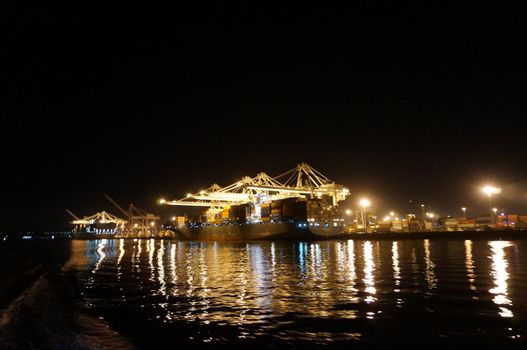 OAKLAND - OCTOBER 12: Fully loaded Shipping Cargo Boats unloaded at night under giants unloading cranes in Oakland Harbor.  Oakland California on October 12, 2015.