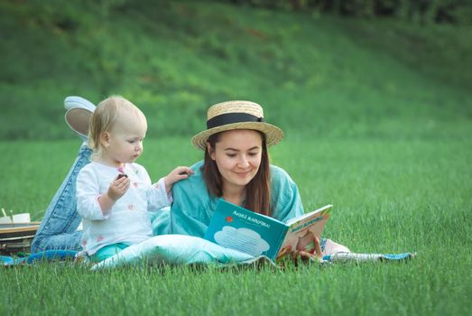 Mother is reading book for baby girl lying on the grass in the park. High quality photo