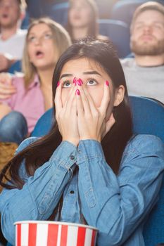 Oh my! Beautiful young asian female covering her mouth with her hands terrified watching a movie at the cinema