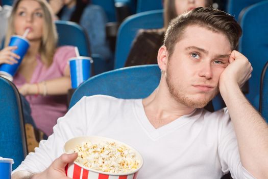 When is it ending? Shot of a young handsome man looking extremely bored watching a movie at the cinema