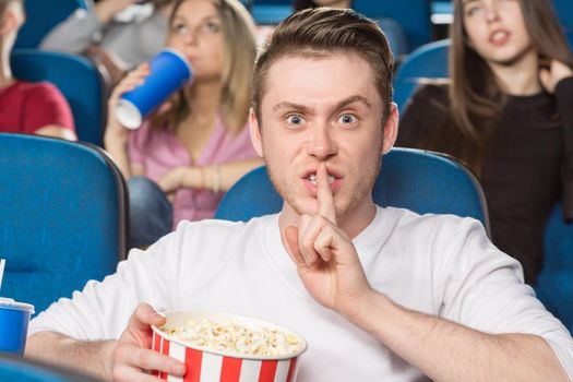 Shut up! Shot of a young annoyed man making shushing gesture looking angrily to the camera at the movie theatre