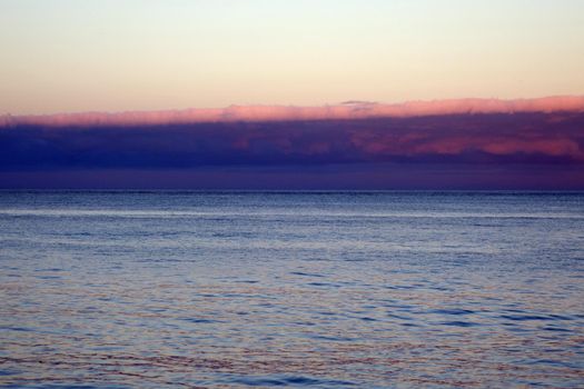 Calm ocean waters of Waimanalo Bay at dusk with clouds hanging overhead on Oahu, Hawaii.                               