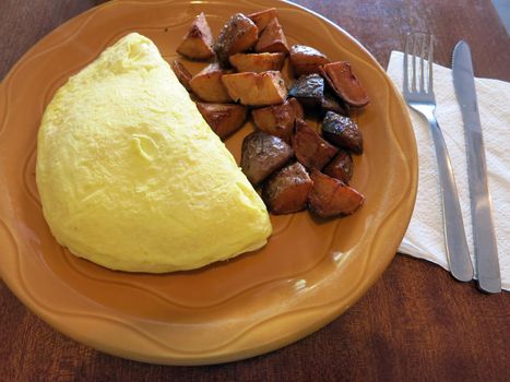 Omelette and Ranch Potatoes on orange plate on a Table with Knife and Fork with napkin. 