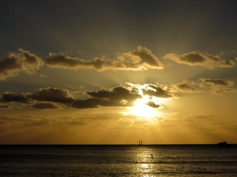 Sunset streams through the clouds with boats on the waters of Waikki on Oahu, Hawaii.