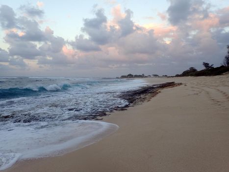 Waves break and crash over lava rocks on Hanakailio Beach with dramatic blue-pink cloudy skyline at dusk on the North Shore of Oahu, Hawaii.  