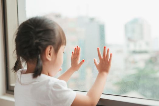 Little asian girl child sitting at home and looking at the window.