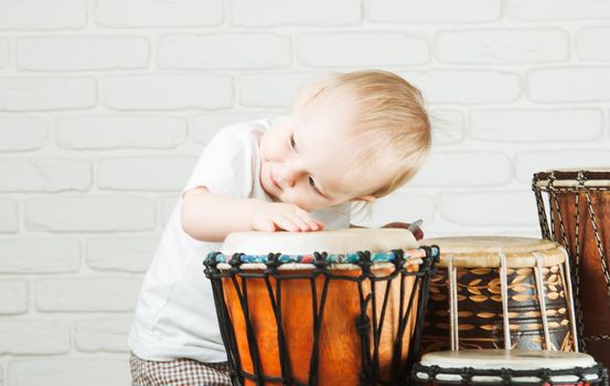 Cute toddler baby playing ethnic drums next to bricks wall