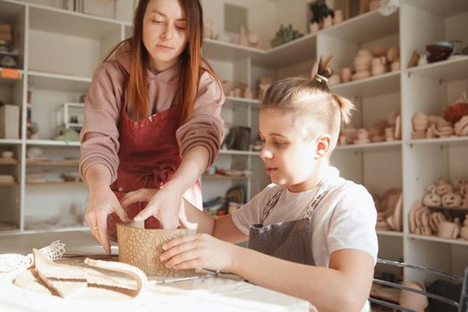 Professional potter helping young boy making tea cup at ceramics class