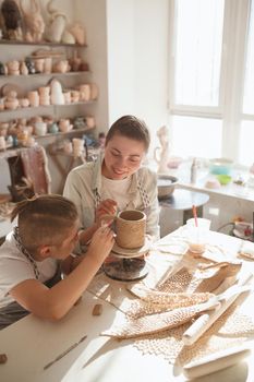 Vertical shot of a happy woman enjoying learning pottery with her young son
