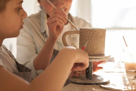 Cropped close up of a ceramic mug being decorated by mother and son at art studio