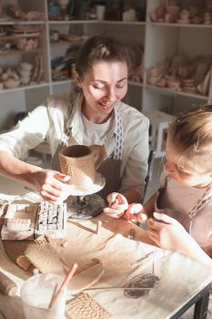 Vertical shot of a charming woman smiling, watching her son decorating ceramic mug they made together