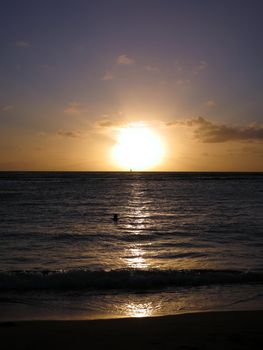 Dramatic Sunset through the clouds and reflecting on the Pacific ocean on the water lapping on the beach in Waikiki of Oahu, Hawaii.