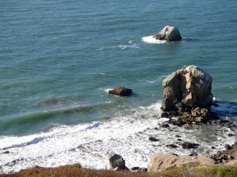 Waves roll toward large rocks and shore on the coast of Marin in California.