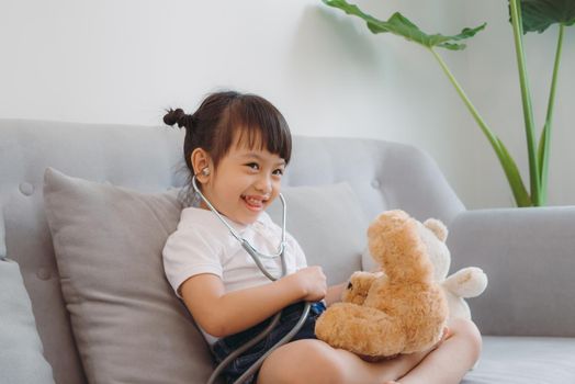 smiling little girl with stethoscope listening to teddy bear breath