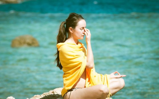 young woman doing yoga breathing pranayama at the blue sea bakcground