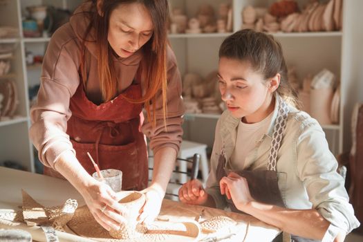 Experienced potter teaching young woman wrking with clay