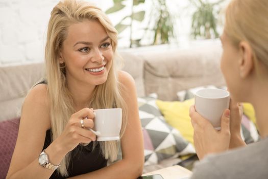 Beautiful young woman having coffee with her female friend smiling happily talking at the cafe girls expressive emotions positivity communication lifestyle leisure morning breakfast sisters togetherness discussion