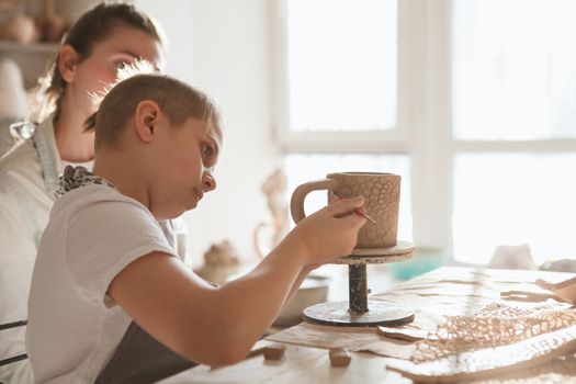 Young boy making ceramic mug with his mother at art class, copy space