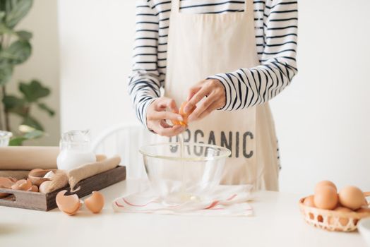 Male hands are breaking an egg into bowl to make dough on white table