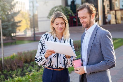 Mature businessman discussing work with his female colleague outdoors. Two business coworkers examining documents in front of business building