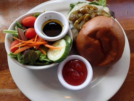 Open jalapeno Pepperjack Cheeseburger with salad featuring lettuce, tomatoes, cucumbers, Carrots with oil and vinegar and side of ketchup.