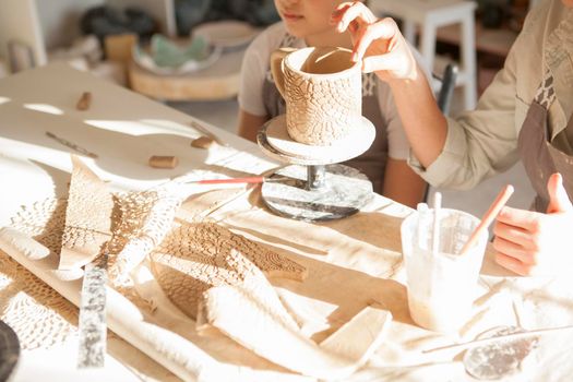Cropped close up of a ceramic mug being made by woman and young boy