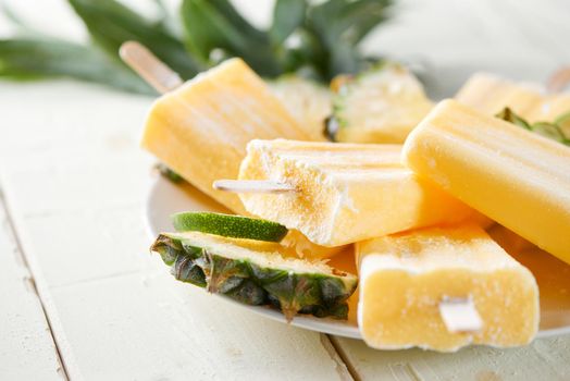 Yellow fruit popsicles on a plate. Top view over a white wood background.