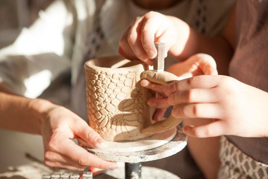 Unrecognizable kid decorating ceramics with stamps, helping mother at pottery class