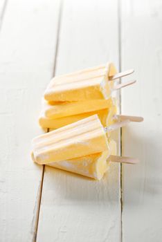 Tall stack of yellow pineapple ice lollies, on a wooden table with white tiled background. Filtered for retro effect