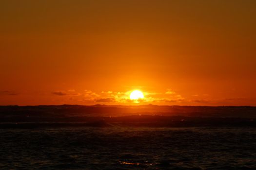 Sunset into the ocean through the clouds and reflecting on the Pacific ocean waves off the coast of Oahu, Hawaii. 2016.