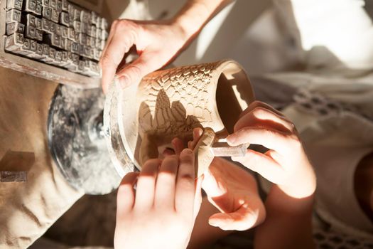 Vertical close up of child helping parent decorating ceramics with stamps