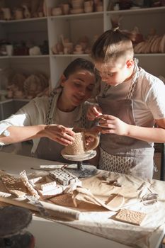 Vertical shot of a charming woman enjoying decorating ceramics with her young son at art workshop